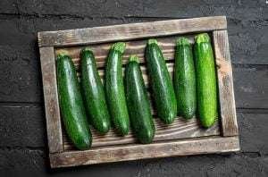 A wooden tray with fresh zucchinis on a black brick wall background