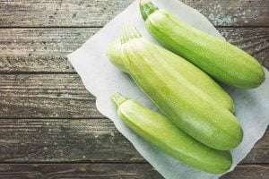 Three light green zucchinis on a white paper towel on a weathered wooden surface
