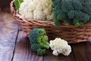 A basket of fresh broccoli and cauliflower on a wooden table