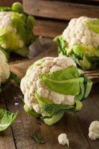 Fresh cauliflowers with green leaves on a rustic wooden table