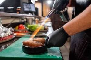 Chef using blowtorch on dish in kitchen cooking sweet potatoes