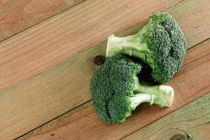 Two fresh green broccoli florets on a light brown wooden surface with knots and holes