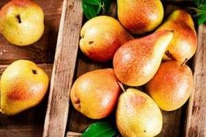 A group of colorful pears in a wooden crate with green leaves on a wooden surface