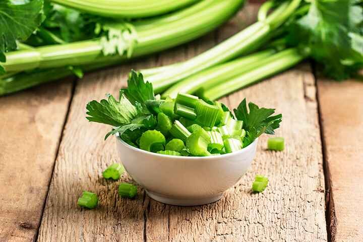 A white bowl of freshly chopped celery on a rustic wooden table