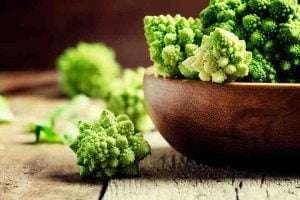 A wooden bowl filled with green Romanesco broccoli and Cauliflower on a rustic wooden table