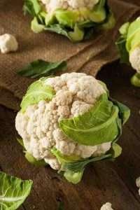 A white head of cauliflower with green leaves on a wooden table, resting on a burlap sack