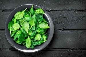 Fresh spinach leaves in a black bowl on a wooden background