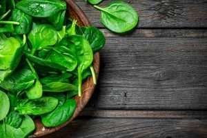 Fresh spinach leaves in a wooden bowl on a dark wooden table, perfect for a healthy horse diet