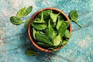 A bowl of fresh spinach leaves on a blue textured background