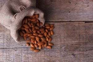 Almonds spilling out of a burlap sack onto a wooden surface