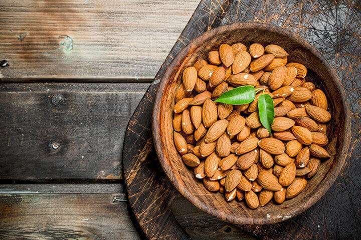 Wooden bowl of almonds with a green leaf on a rustic wooden table