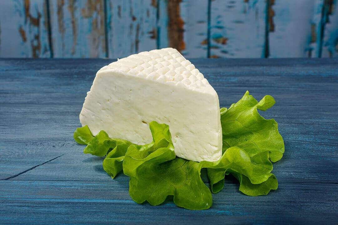 White cheese on a bed of fresh green lettuce leaves on a blue wooden surface