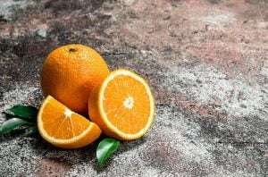 Can Horses Eat Oranges?, A whole orange and two orange slices with green leaves on a textured gray background