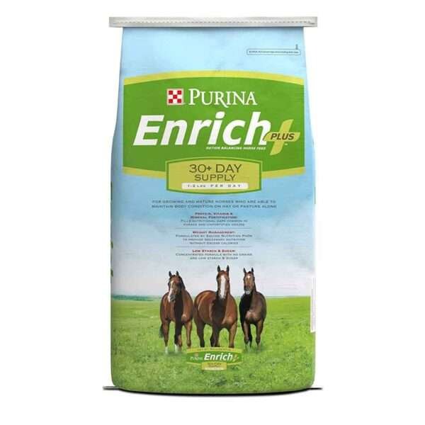 A bag of Purina Enrich Plus horse feed in a light blue color with a white stripe. The bag has a picture of three horses and claims to be a 30+ day supply for growing and mature horses, low starch and low sugar. The background is a green field with blue sky